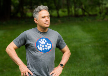 A man in grey shirt standing on grass next to trees.