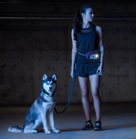 A woman and her dog are standing in the dark.