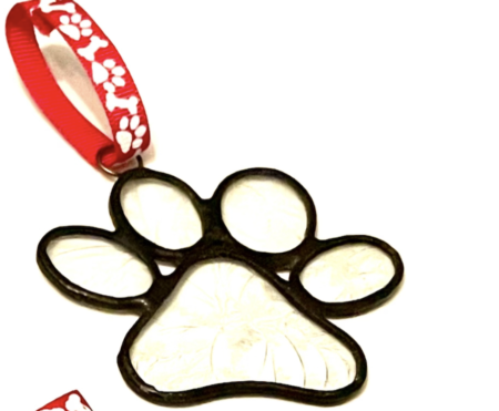 A paw print ornament hanging from a red ribbon.