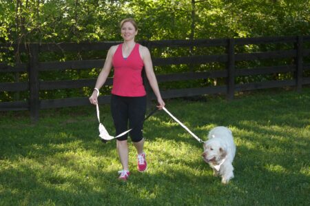 A woman walking her dog in the grass.